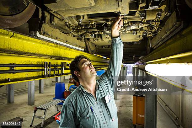 Belgian male mechanic performs maintenance work in the pit workshop underneath a De Lijn tram in the company depot in Gentbrugge, Ghent, Belgium.