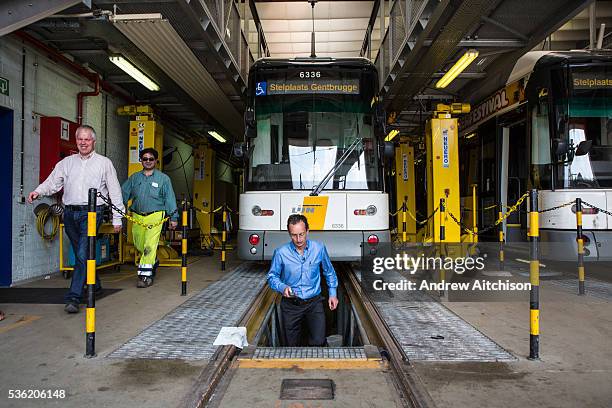 Patrick De Boeuf, Chief Executive of De Lijn, steps up from the pit workshop area beneath a modern tram two males walk along side the tram in the...