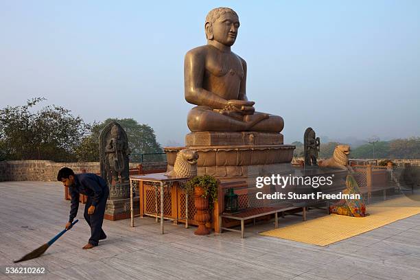Man sweeps whilst a woman prays at dawn at the statue of Lord Mahavira at the Ahinsa Sthal Jain temple, Delhi, India