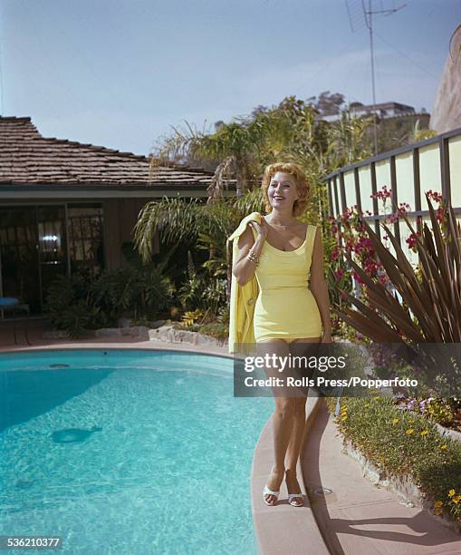 American actress Rhonda Fleming pictured wearing a lemon yellow swimsuit with matching jacket beside a domestic swimming pool in the United States...