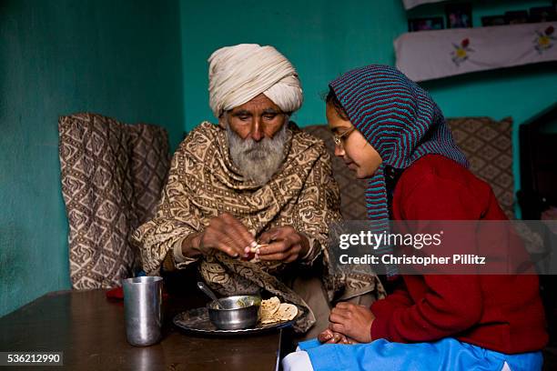 Young Punjabi girl, Jasbir Kaur, being feed breakfast by her grandfather at home, Chita Kallan village, Punjab, India | Location: Chita Kalaan...