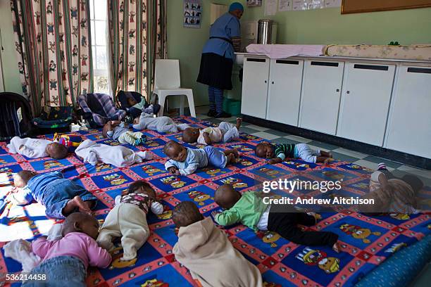 Many babies lying and playing on a large mattress on the floor while their carer washes her hands at Princess Alice's Adoption Home, Guateng, South...