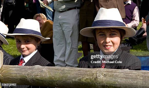 Young boy dressed in pin striped suit and tie and hat behind fence near starting grid