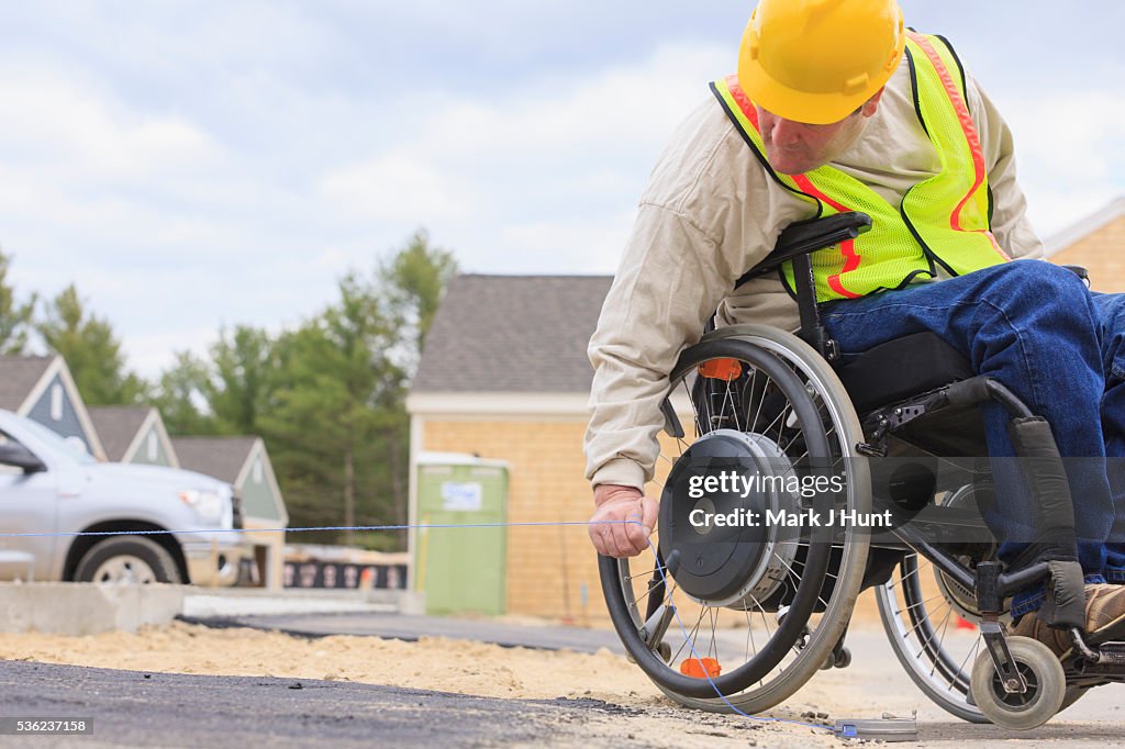 Construction supervisor with Spinal Cord Injury pulling chalkline at edge of pavement