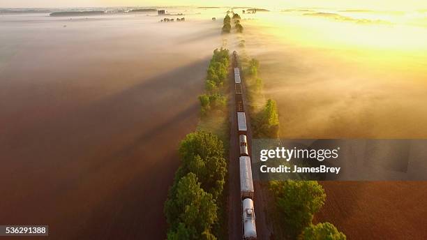 freight train rolls through fog, across breathtaking landscape at sunrise. - aerial train stock pictures, royalty-free photos & images