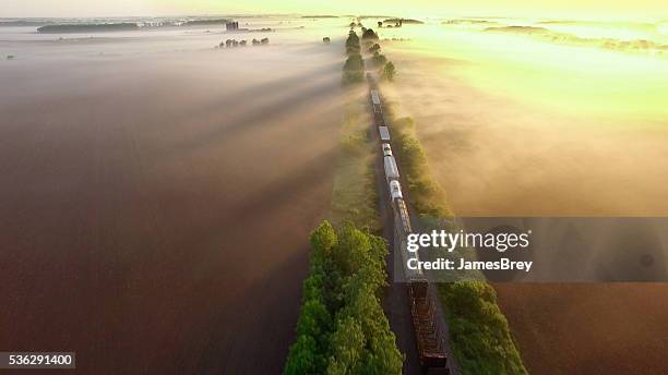 freight train rolls across surreal, foggy landscape at sunrise - aerial train stock pictures, royalty-free photos & images