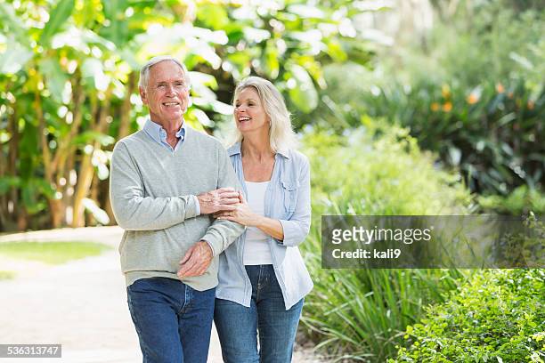 portrait of senior couple walking in the park - arm in arm stock pictures, royalty-free photos & images
