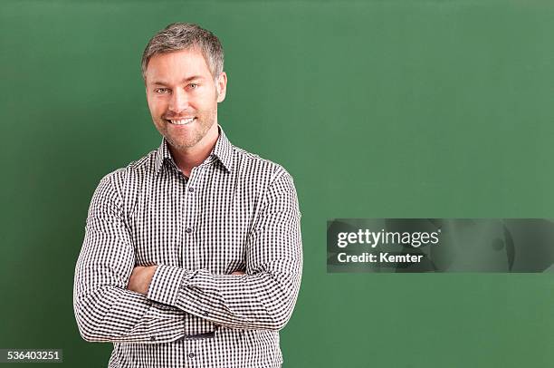 smiling teacher with arms crossed standing at blackboard - teacher man bildbanksfoton och bilder