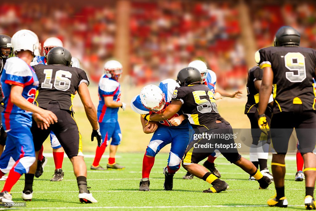 Football team's running back carries ball. Defenders. Stadium fans. Field.