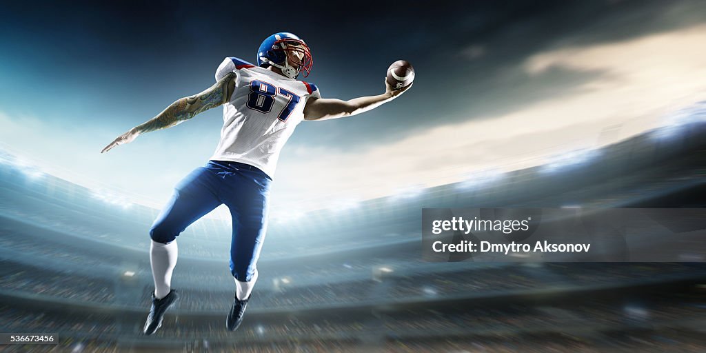 American football player catching ball mid air in stadium