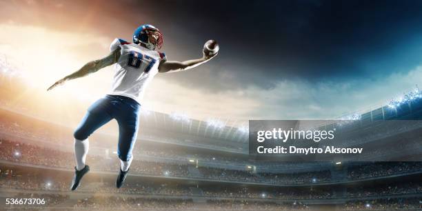 american football player catching ball mid air in stadium - catcher stock pictures, royalty-free photos & images