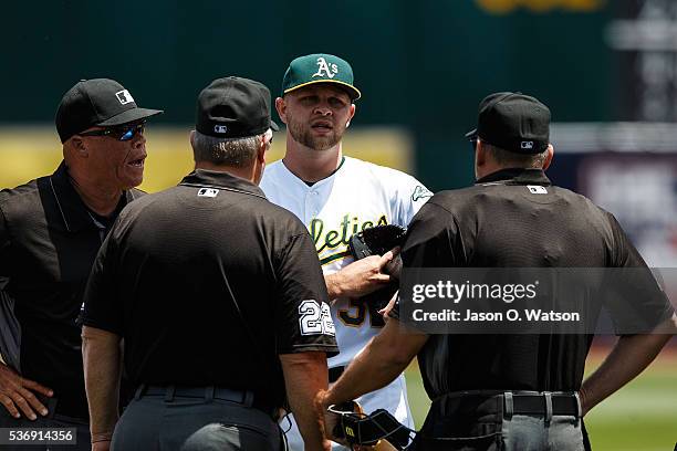 Umpires Kerwin Danley, Joe West and Andy Fletcher talk to Jesse Hahn of the Oakland Athletics about a uniform violation during the first inning...