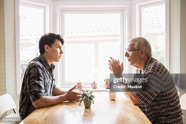 side view of grandfather and grandson communicating while having coffee - generationsunterschied stock-fotos und bilder