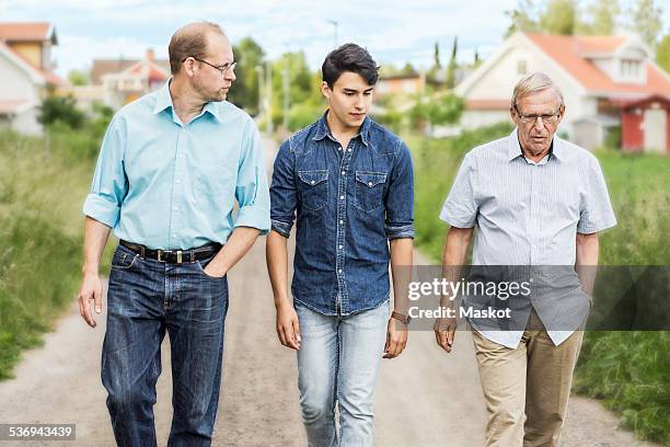 three generation males walking together on footpath - dreiviertel vorderansicht stock-fotos und bilder