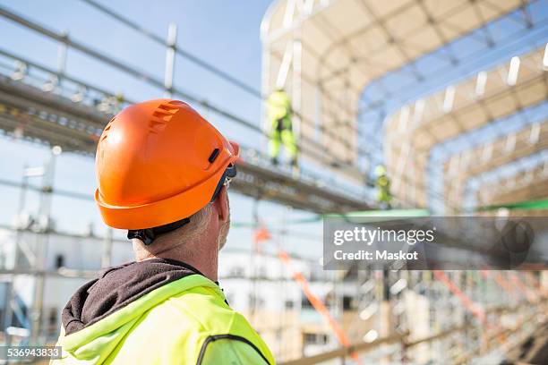 rear view of worker looking at colleagues working at construction site - baustelle gerüst sonne stock-fotos und bilder