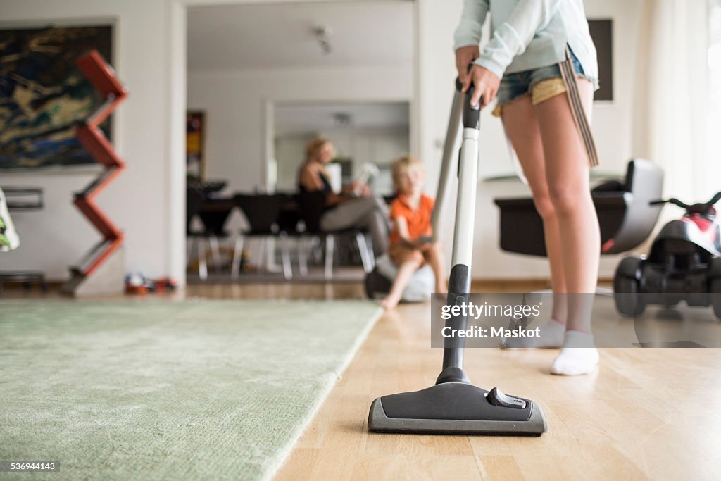 Low section of girl cleaning floor with vacuum cleaner at home
