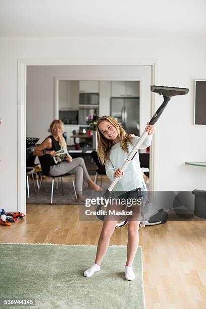 full length portrait of playful girl holding vacuum cleaner at home with mother sitting in background - doing household chores stock pictures, royalty-free photos & images