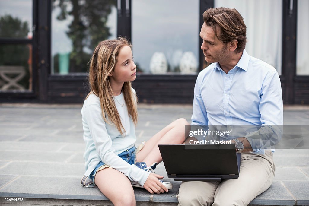 Father and daughter discussing while using laptop at porch
