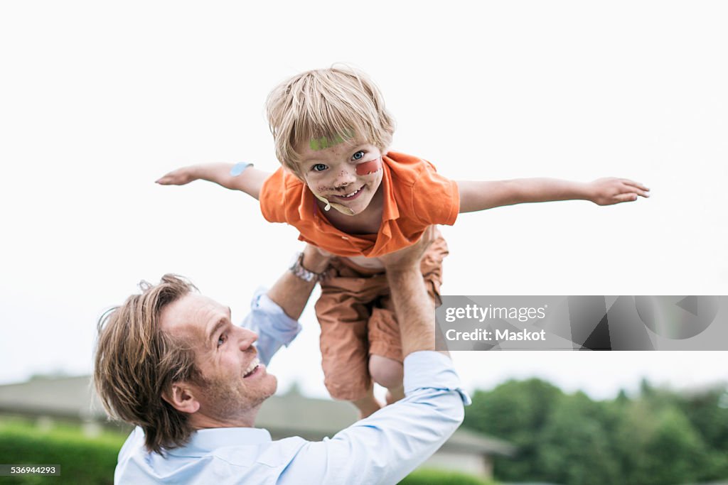 Playful father lifting injured son against clear sky