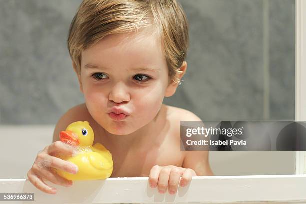 blonde boy playing with rubber duck in bathtub - badeend stockfoto's en -beelden