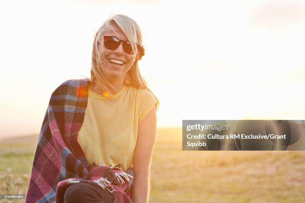 Young woman wrapped in blanket in rural field at sunset, Dorset, England