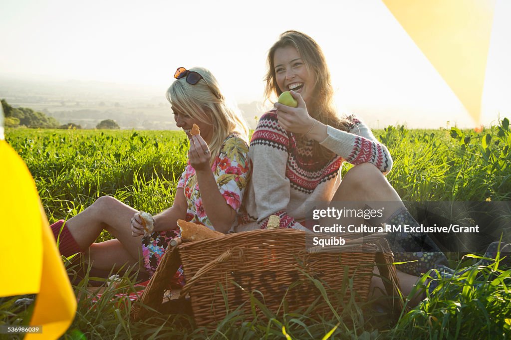 Two young women friends sharing picnic in rural field