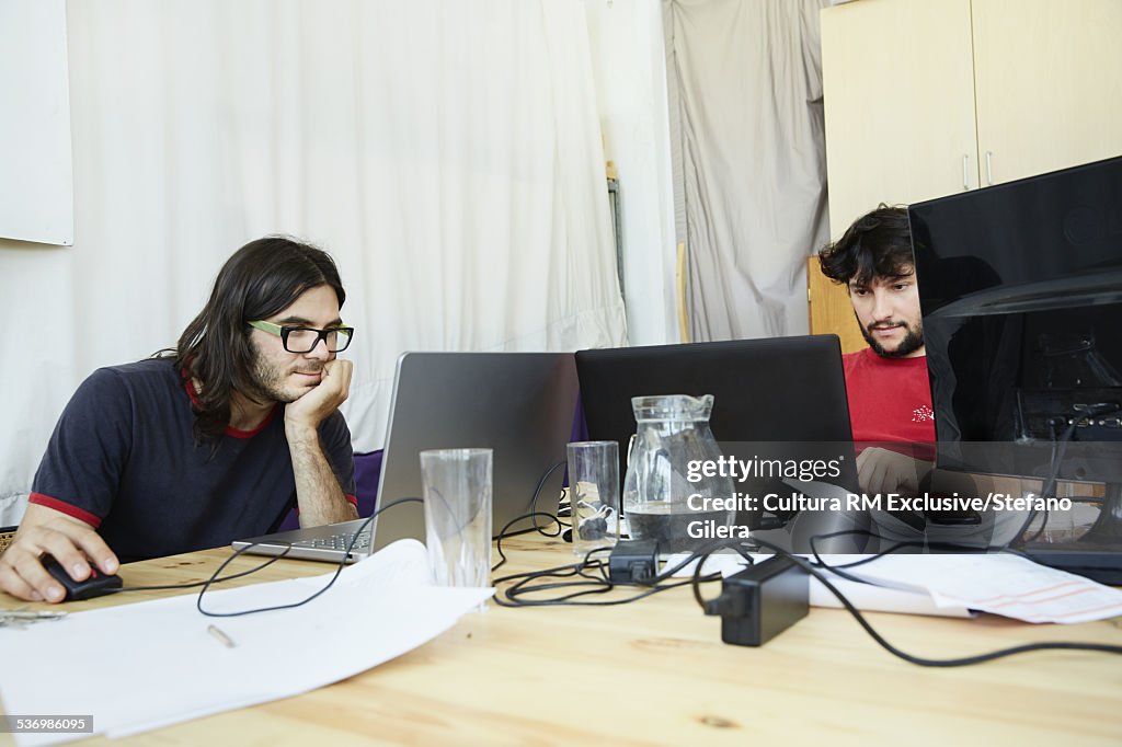 Two male office workers working on laptops in office