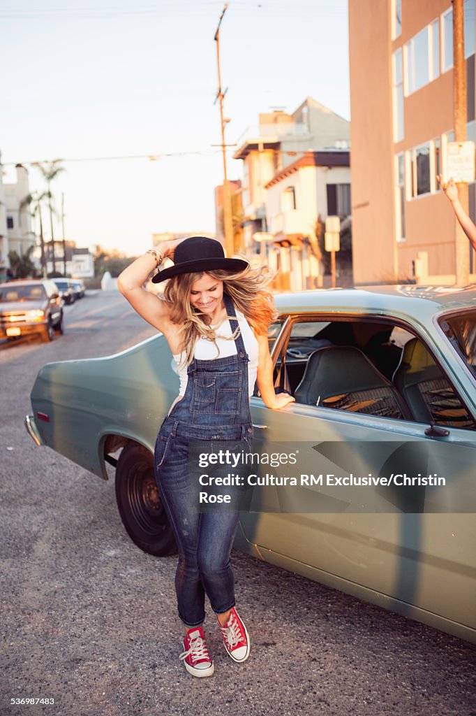 Young woman wearing dungarees by car in street