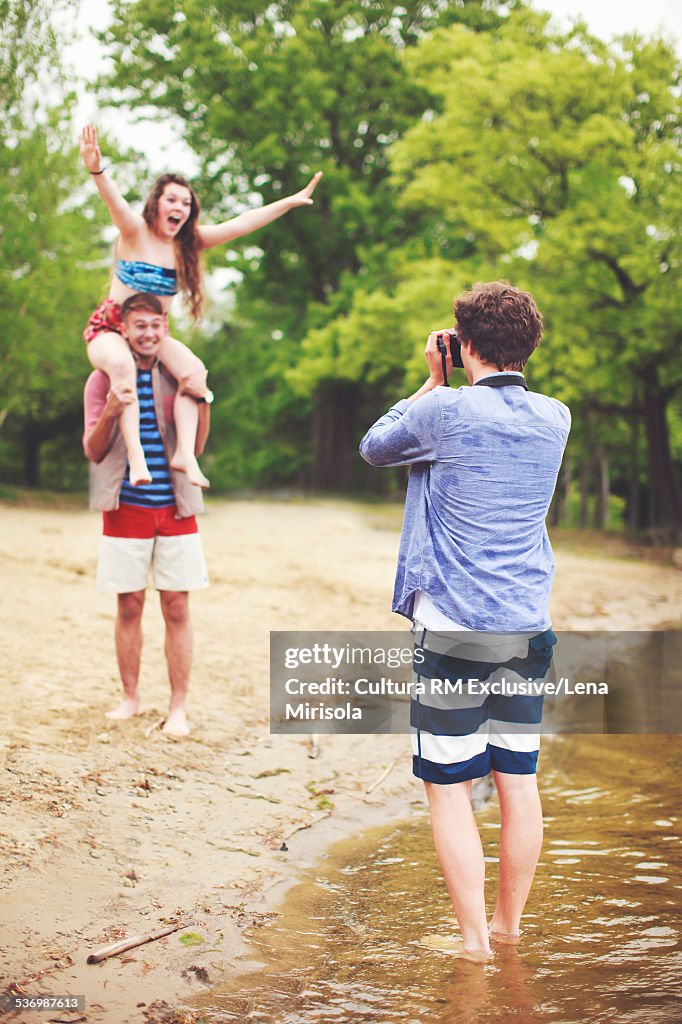 Young man taking photo of friend carrying woman on shoulders