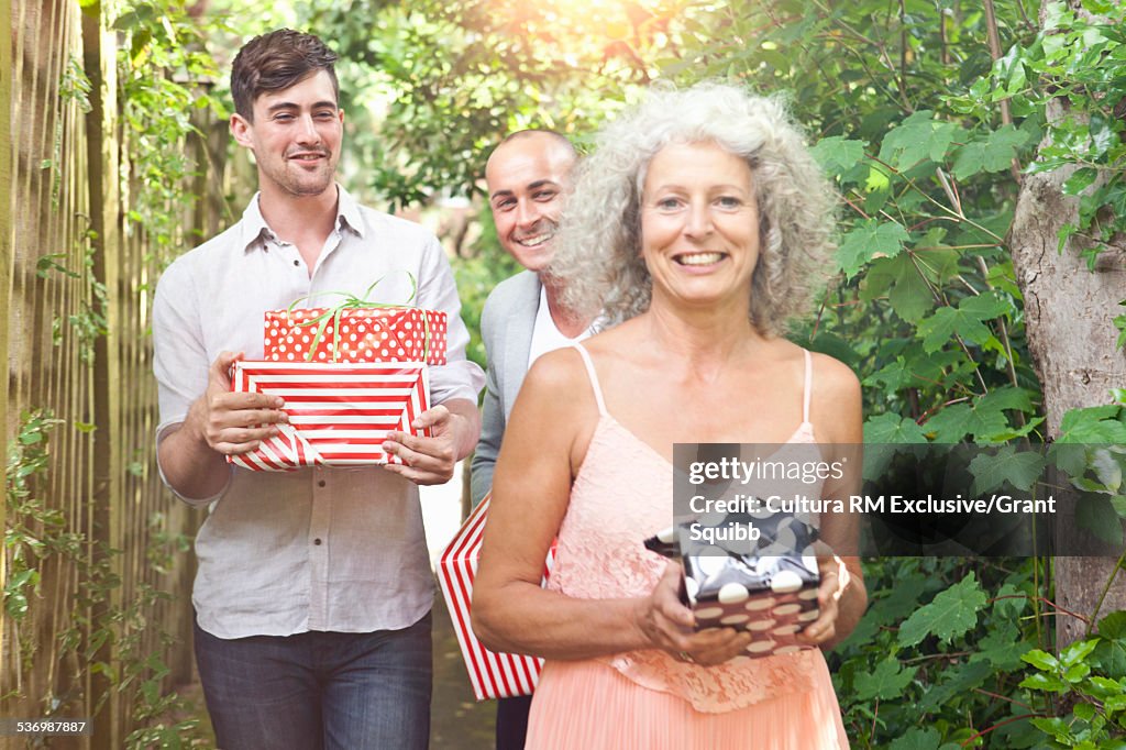 Mother and sons carrying gifts along garden path for surprise birthday party