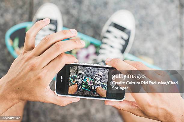 cropped shot of young male skateboarder photographing feet on smartphone - skate sports footwear stock-fotos und bilder