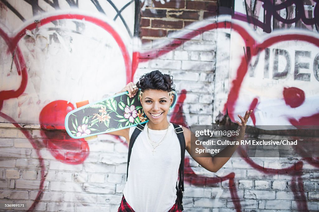 Portrait of young woman skateboarder and graffiti wall