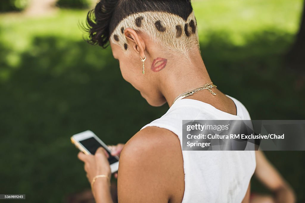 Over shoulder view of young woman texting on smartphone in park