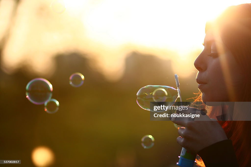 Netherlands, Amsterdam, Side view of young woman blowing bubbles