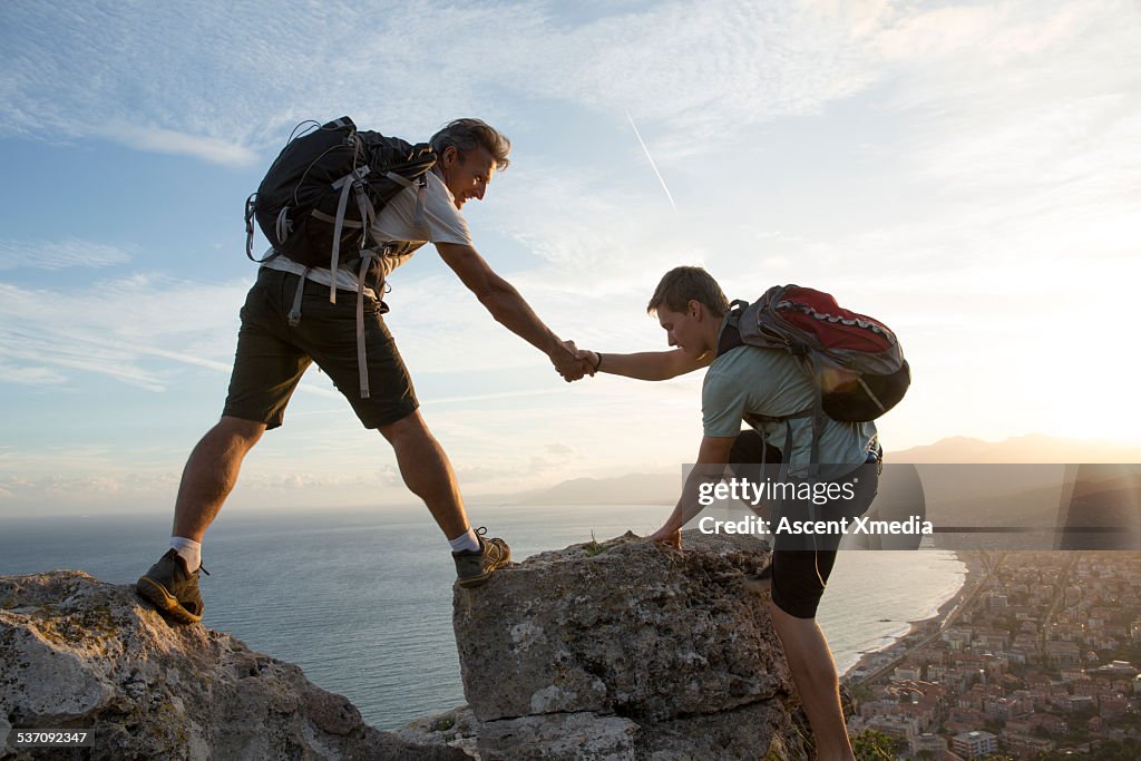 Father helps son to pinnacle summit, village below