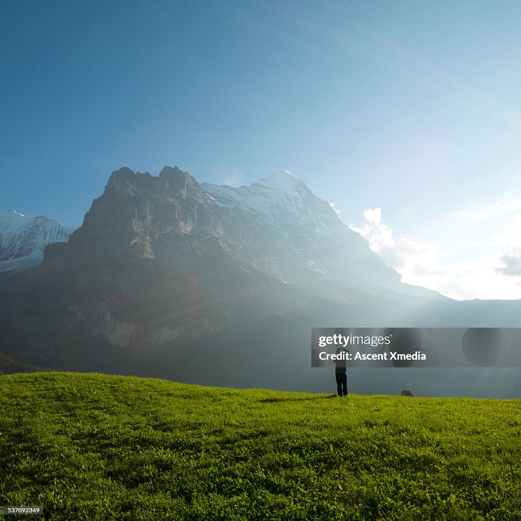 Man takes photo from green meadow, towards Eiger