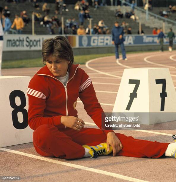 Sprinterin DDR, sitzt vor einem Startblock vor einem, Wettkampf und macht sich warm, - o.J.