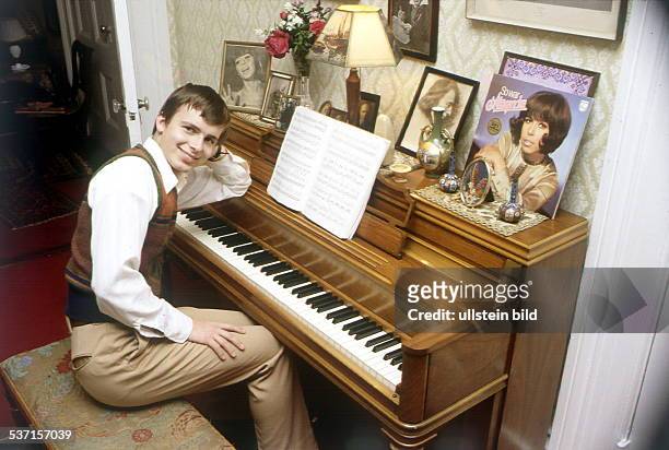 Sitzt zu Hause in den USA am Klavier, auf dem die LP seiner Mutter steht: 'So war Alexandra', - ohne Jahr