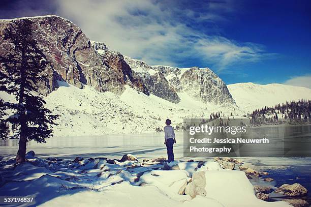 woman standing with frozen lake and snowy mountain - laramie foto e immagini stock