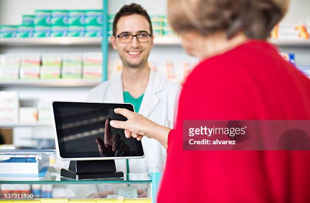 farmacêutico no pagamento salão com cliente pagar através de tablet digital - female pharmacist with a digital tablet imagens e fotografias de stock