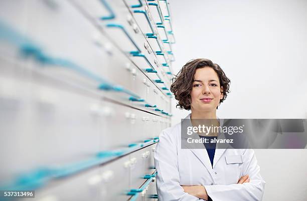 confident young pharmacist standing by a medicine shelf - cure berlin 2016 stock pictures, royalty-free photos & images