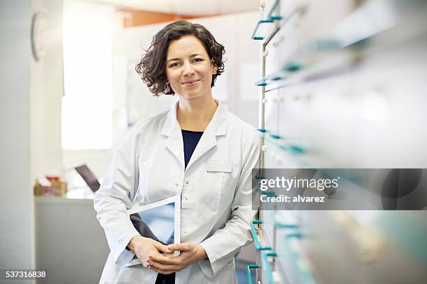 pharmacist leaning to a medicine shelf with digital tablet - pharmacy stockfoto's en -beelden