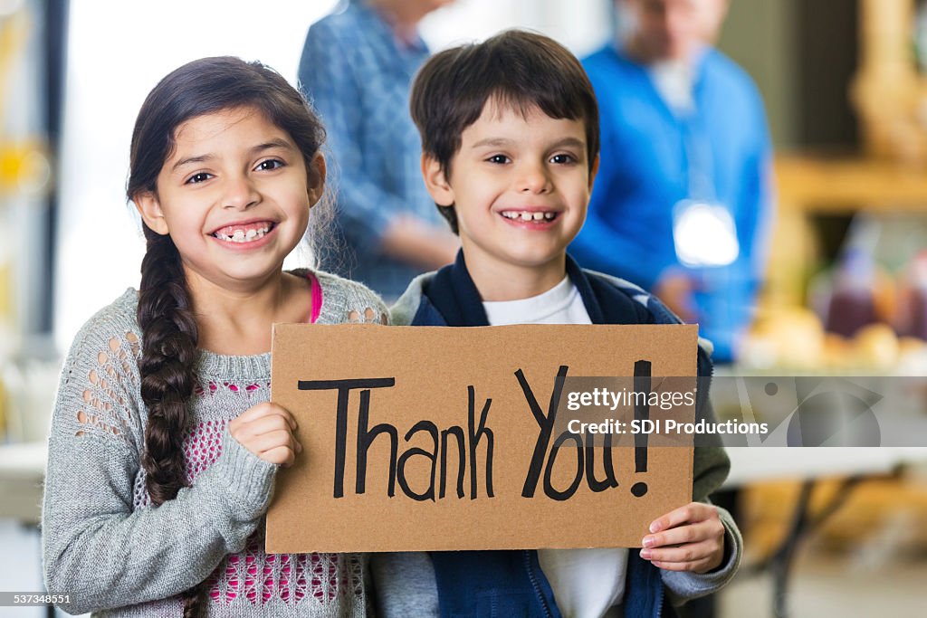 Smiling children holding a thank you sign out of food bank.