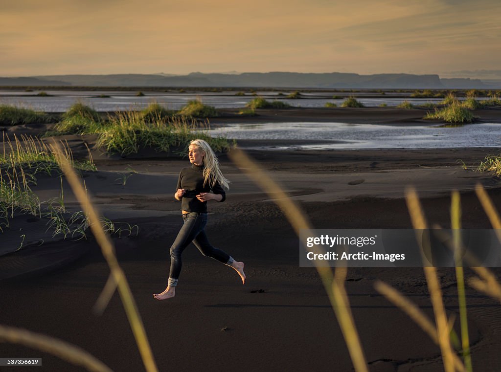 Woman running on black sand beach.