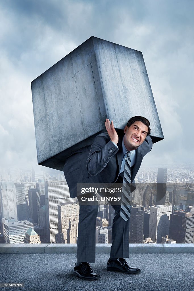 Businessman Struggling Under Weight Of Concrete Block