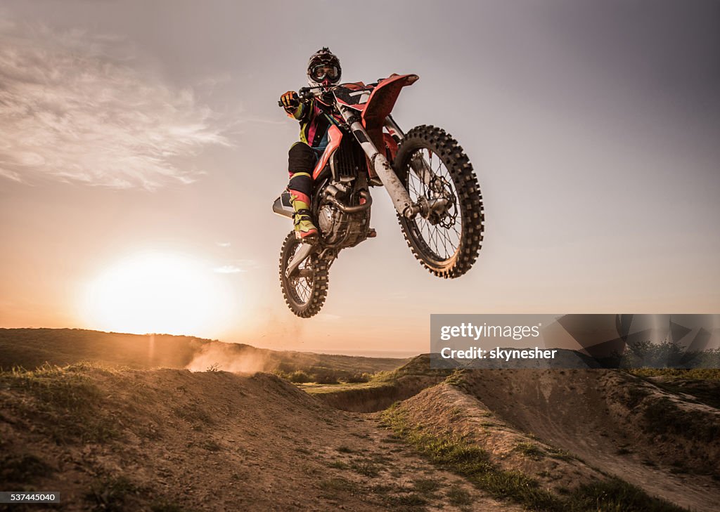 Piloto de Motocross realiza salto de altura al anochecer.