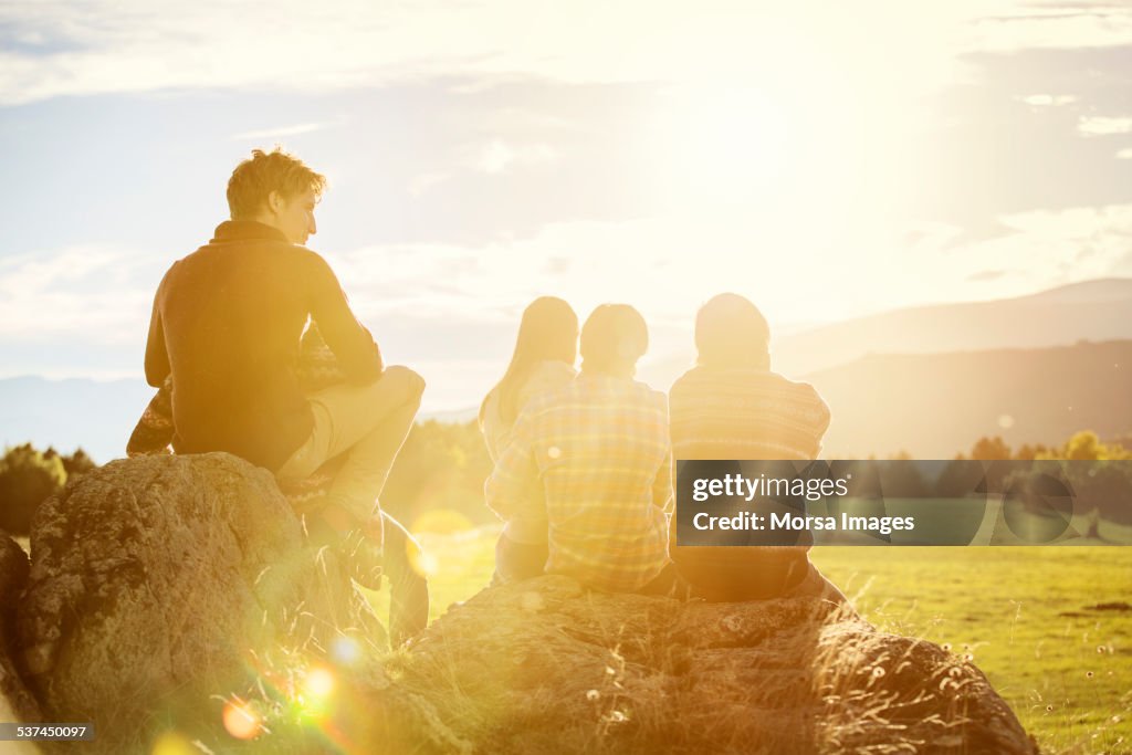 Friends relaxing on rock at field