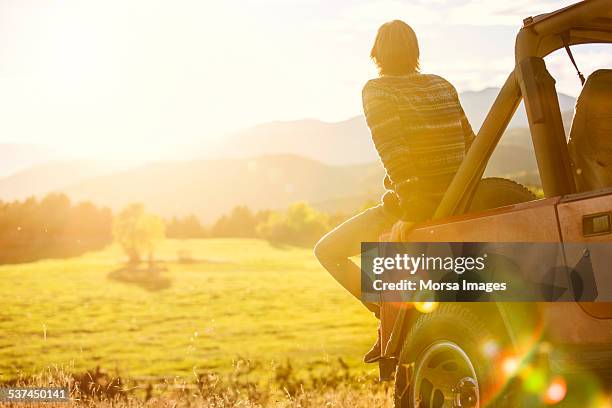 man sitting on back of suv parked at field - sunny photos et images de collection