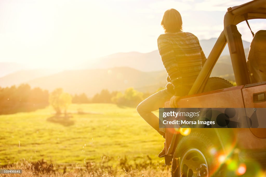 Man sitting on back of SUV parked at field