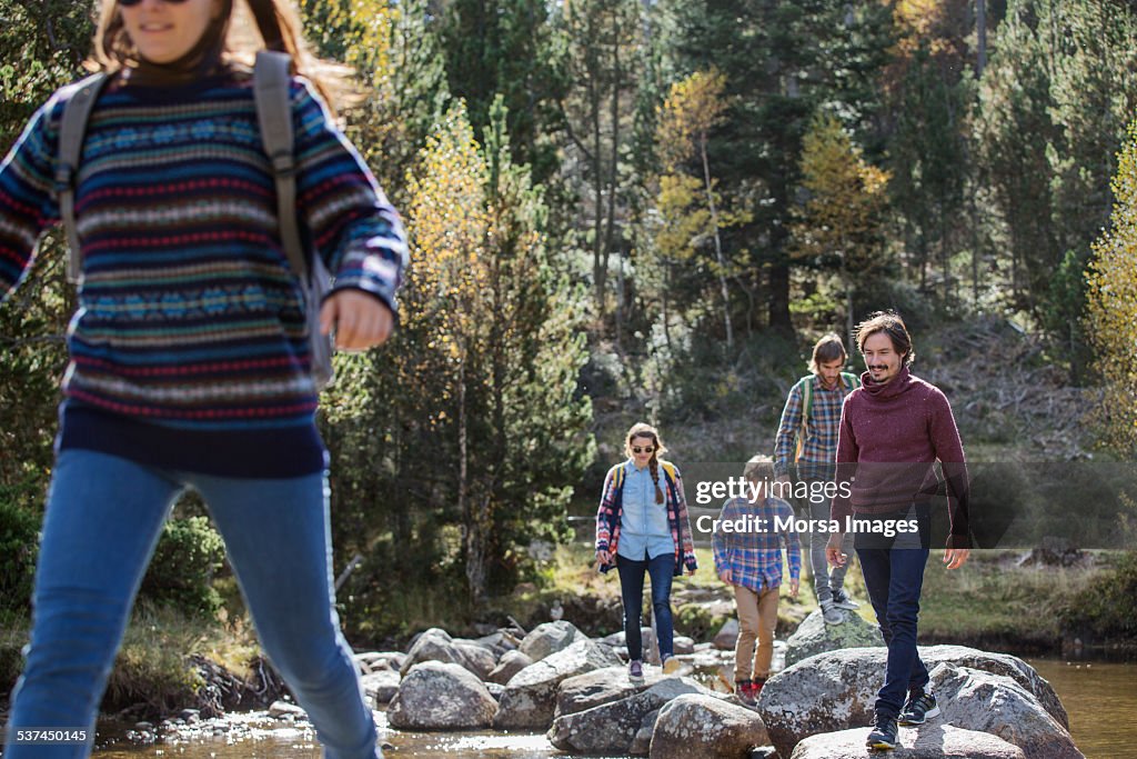 Friends crossing rocks at river in forest